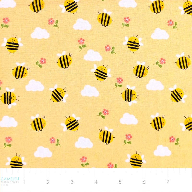 Camelot Fabrics Bumble Bees peach cotton flannel fabric featuring cheerful yellow bees, fluffy clouds, and pink flowers from the Fleece and Flannel 2026 Collection.