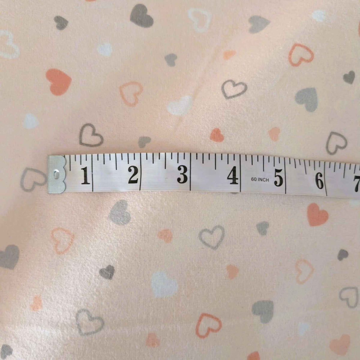 Pearl pink printed cotton flannel fabric with scattered pastel heart design by Robert Kaufman with tape measure