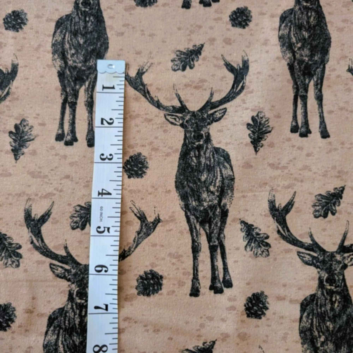 Cotton flannel fabric with stag deer, oak leaves, and pinecones on a rustic beige background, brushed for softness, Oeko-Tex certified.