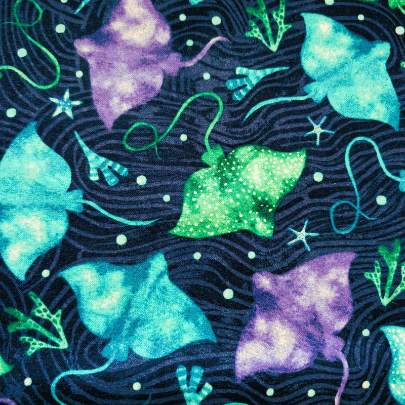 Cotton flannel fabric with colorful stingrays in blue, green, and purple on a dark ocean background with seaweed and starfish. Brushed soft, OEKO-TEX certified, 44 inches wide.