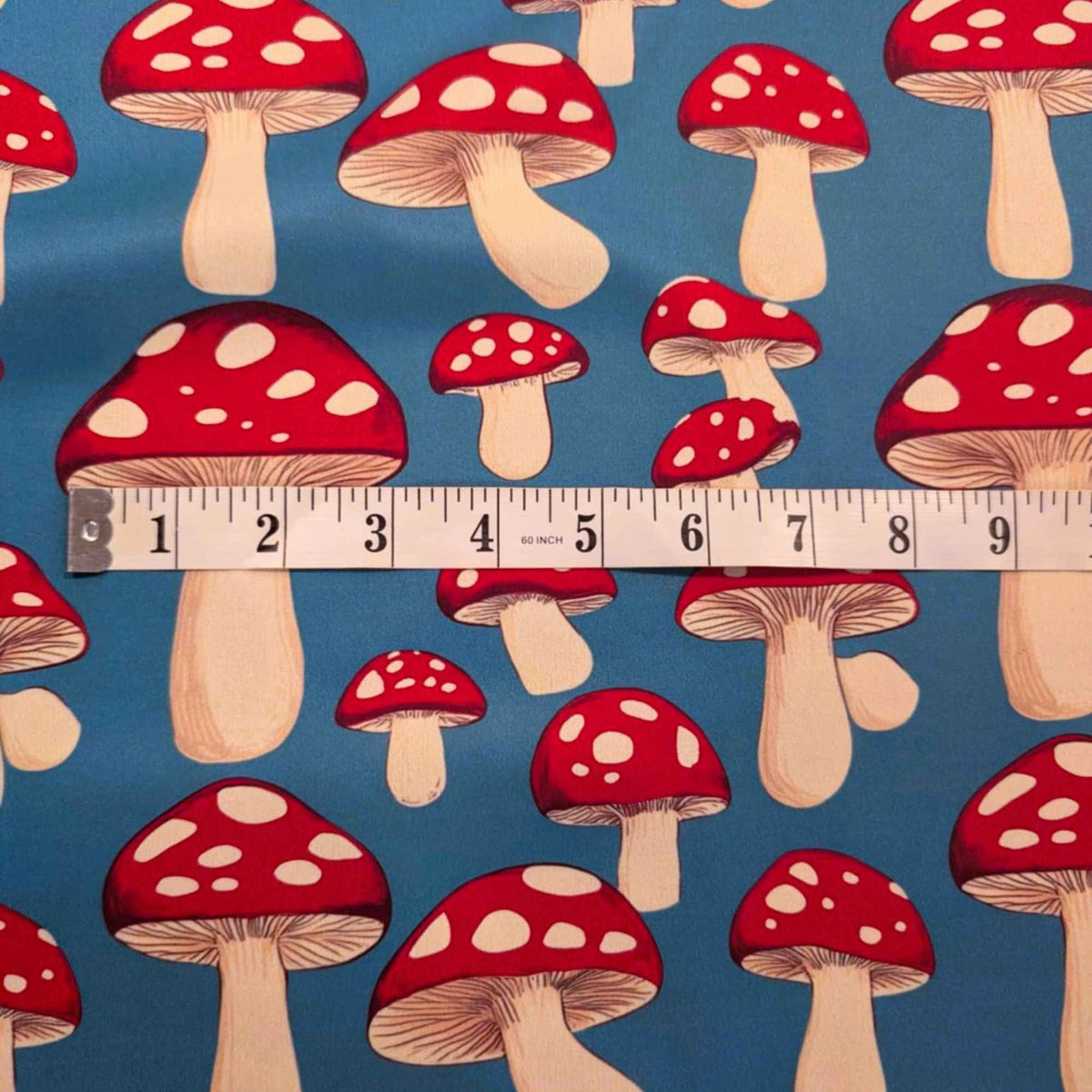 Red toadstool mushroom print food safe waterproof PUL fabric on blue background with white spotted mushrooms.