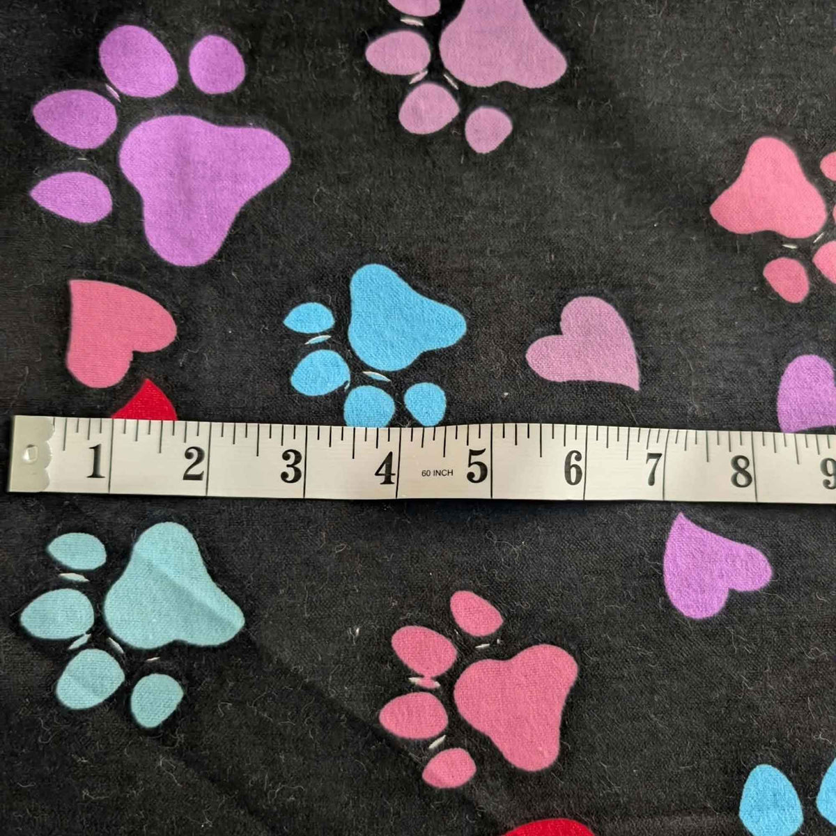 Black cotton flannel fabric with scattered paw prints and hearts in pink, purple, red, turquoise and aqua