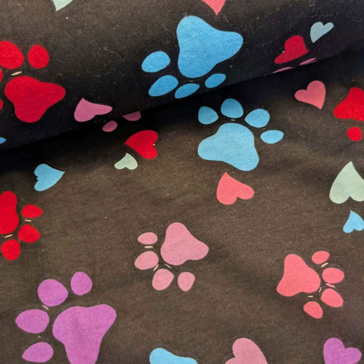 Black cotton flannel fabric with scattered paw prints and hearts in pink, purple, red, turquoise and aqua