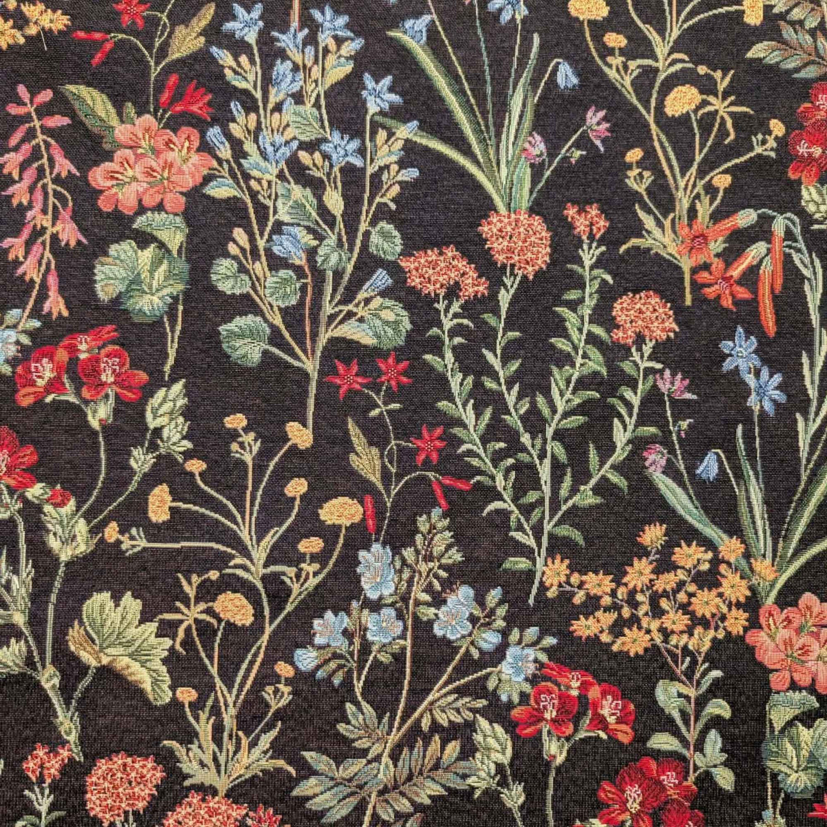 Botanical wildflower Gobelin tapestry fabric with red, coral, blue and yellow flowers and sage green leafy stems on a black background.