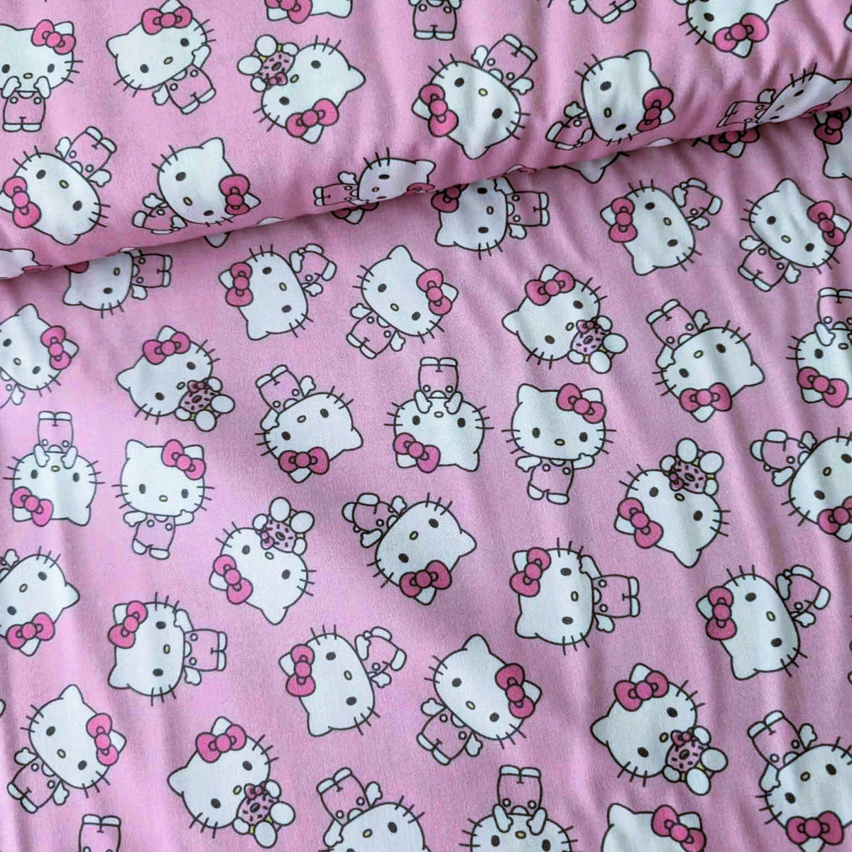 Officially licensed Hello Kitty cotton fabric by Springs Creative featuring an all-over toss of Hello Kitty holding a teddy bear on a pink background.