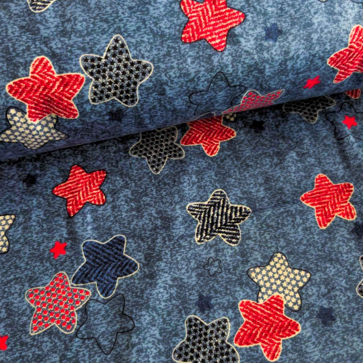 Star print cotton flannel with red, navy, black and cream patterned stars on a textured denim-look blue background.