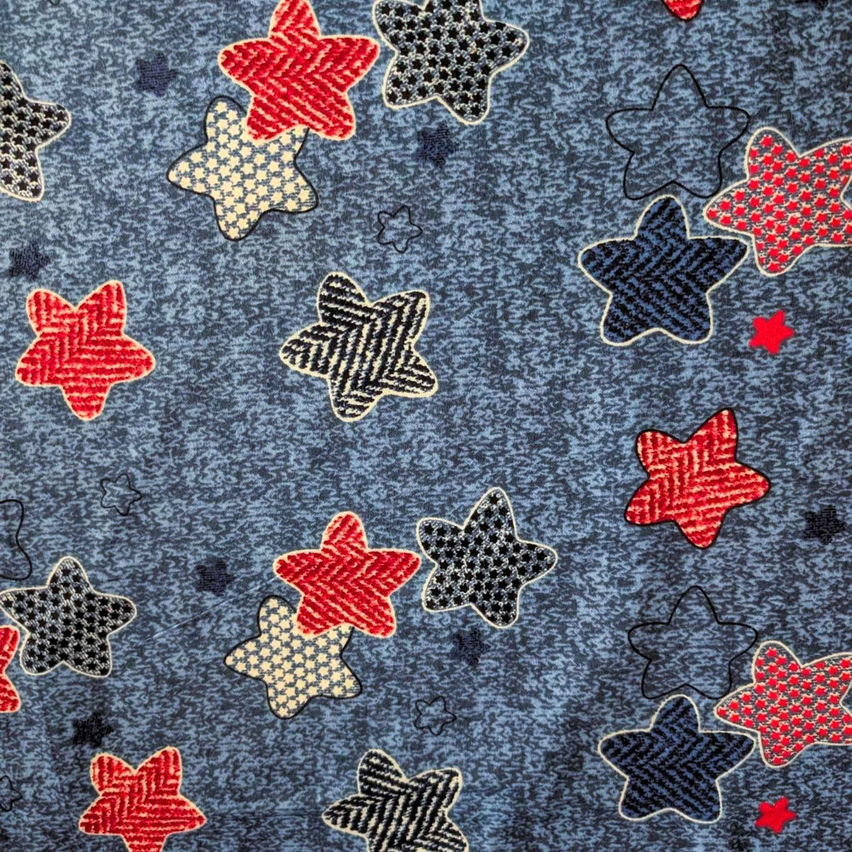 Star print cotton flannel with red, navy, black and cream patterned stars on a textured denim-look blue background.