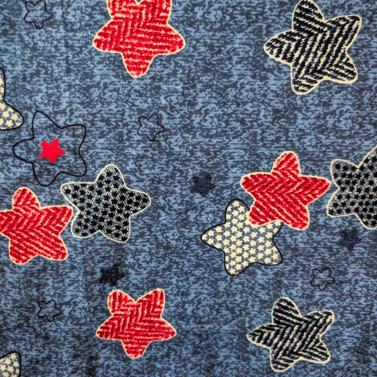 Star print cotton flannel with red, navy, black and cream patterned stars on a textured denim-look blue background.