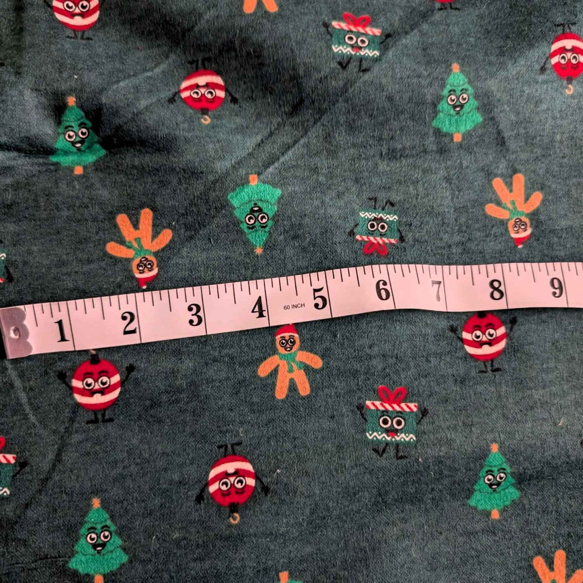 Dark green cotton flannel with smiling Christmas trees, gingerbread figures, red and white ornaments, and gift boxes.