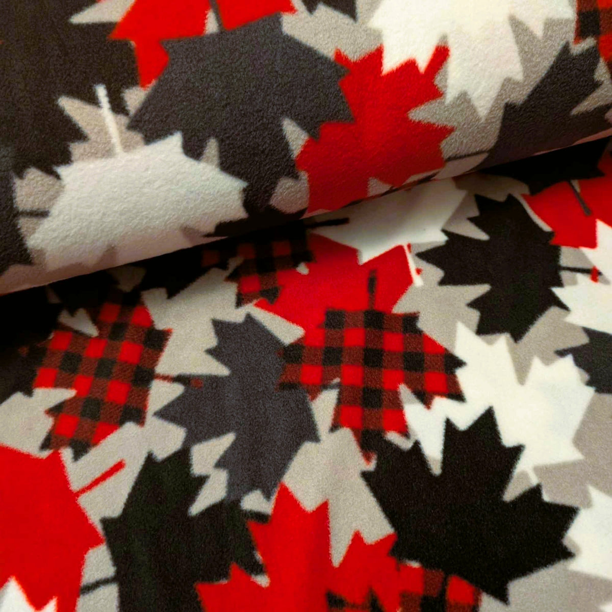 Maple Leaves fleece by Camelot with overlapping red, black, grey and white leaves, including red and black plaid maple leaves.
