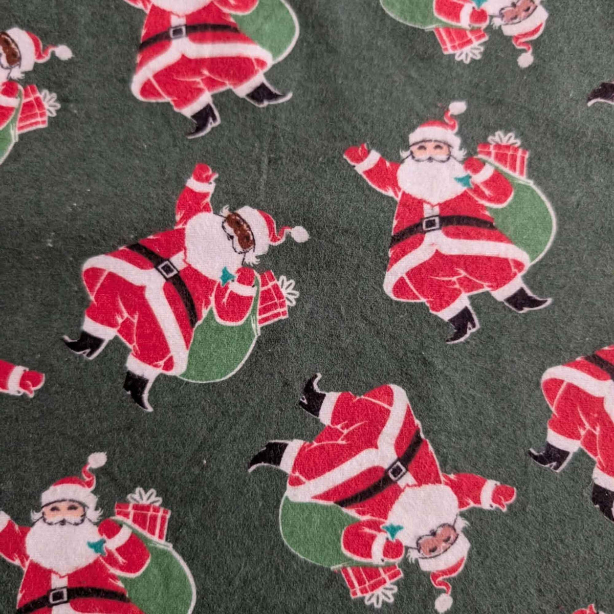 Dark green cotton flannel fabric with tossed Santa Claus figures in red suits carrying green sacks with wrapped presents.