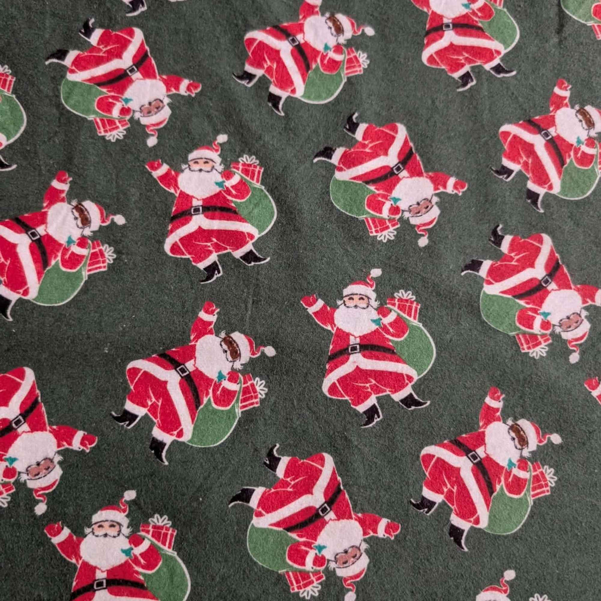 Dark green cotton flannel fabric with tossed Santa Claus figures in red suits carrying green sacks with wrapped presents.