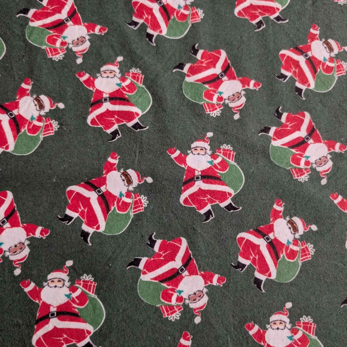 Dark green cotton flannel fabric with tossed Santa Claus figures in red suits carrying green sacks with wrapped presents.