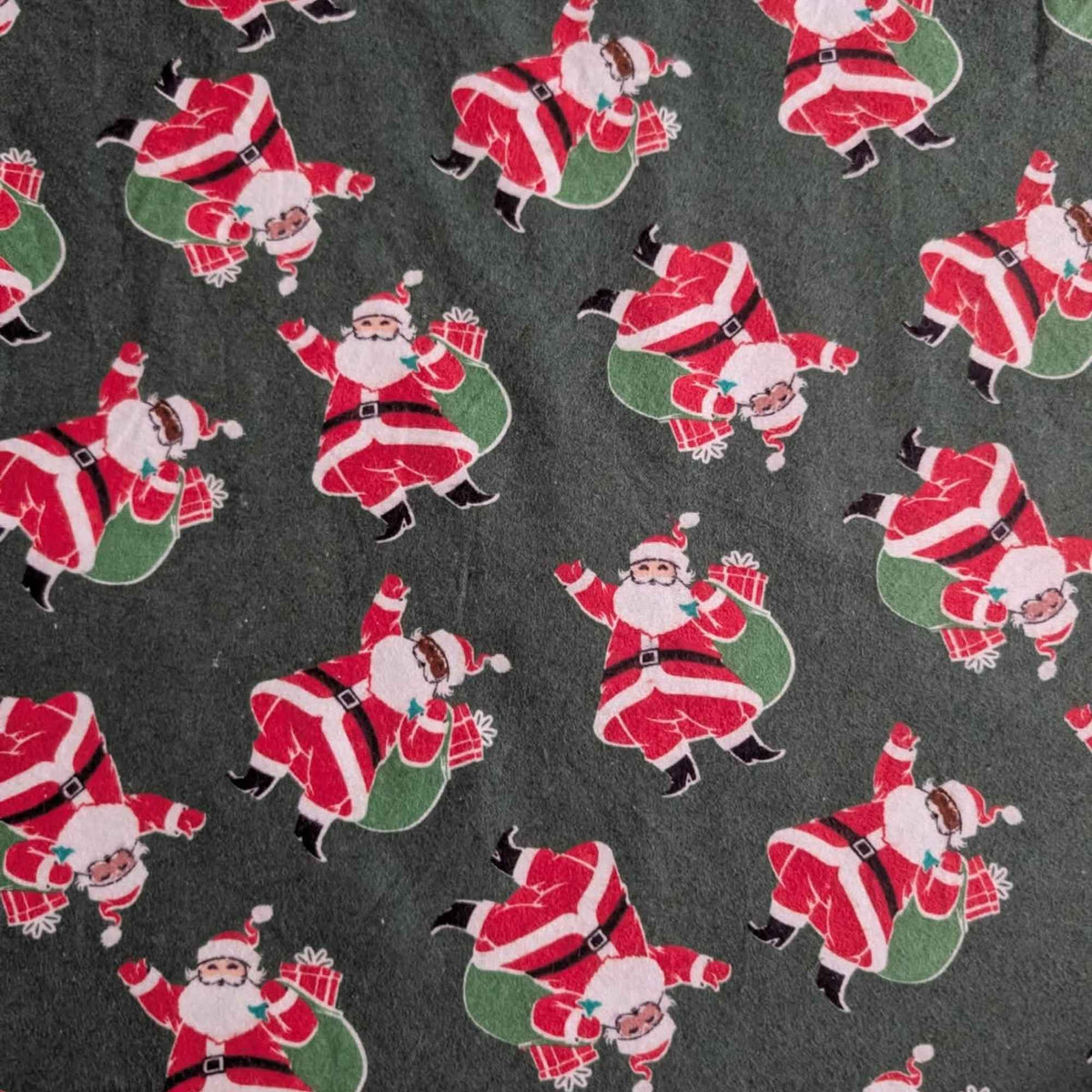 Dark green cotton flannel fabric with tossed Santa Claus figures in red suits carrying green sacks with wrapped presents.