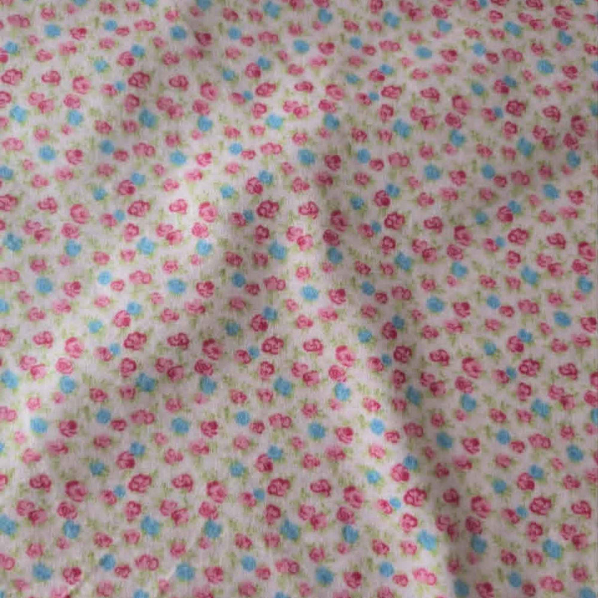Double brushed flannel fabric featuring tiny pink rosebuds, soft blue flowers, and green foliage scattered across a pink background.