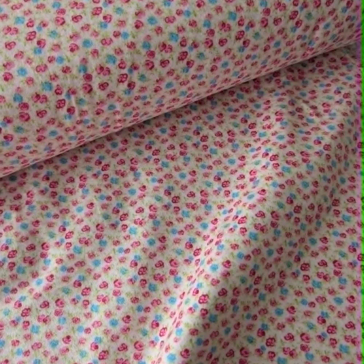 Double brushed flannel fabric featuring tiny pink rosebuds, soft blue flowers, and green foliage scattered across a pink background.