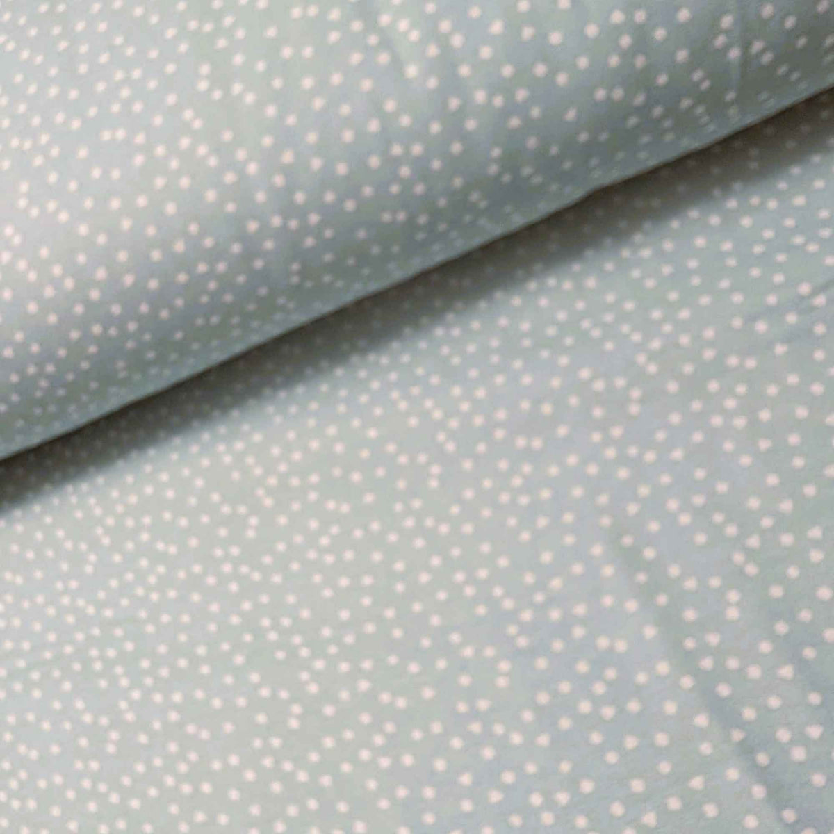 A close-up of a light sage green fabric with a white polka dot pattern, folded to show its texture and color.