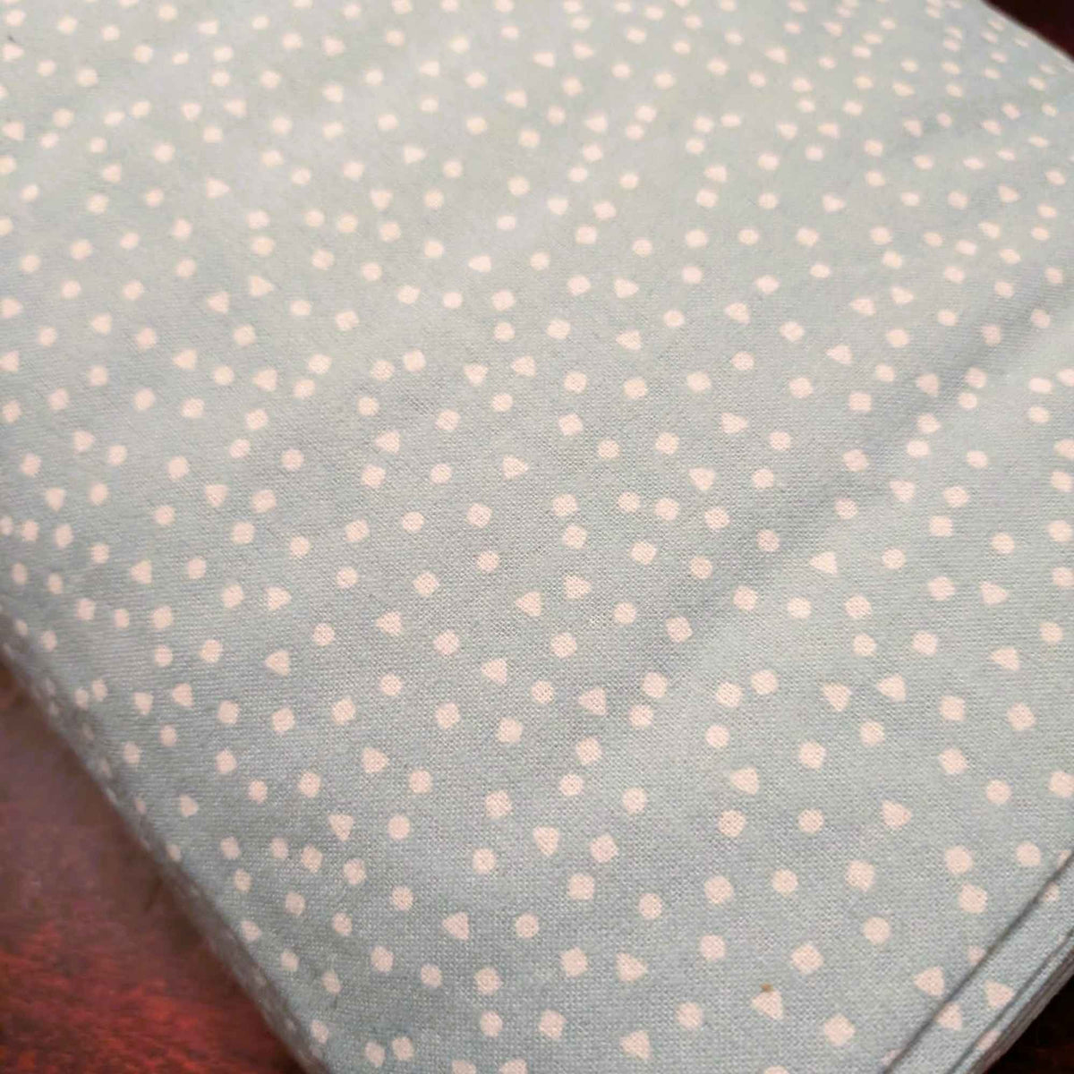 A close-up of a light sage green fabric with a small white geometric pattern of dots, triangles, and squares, folded over to show its texture.