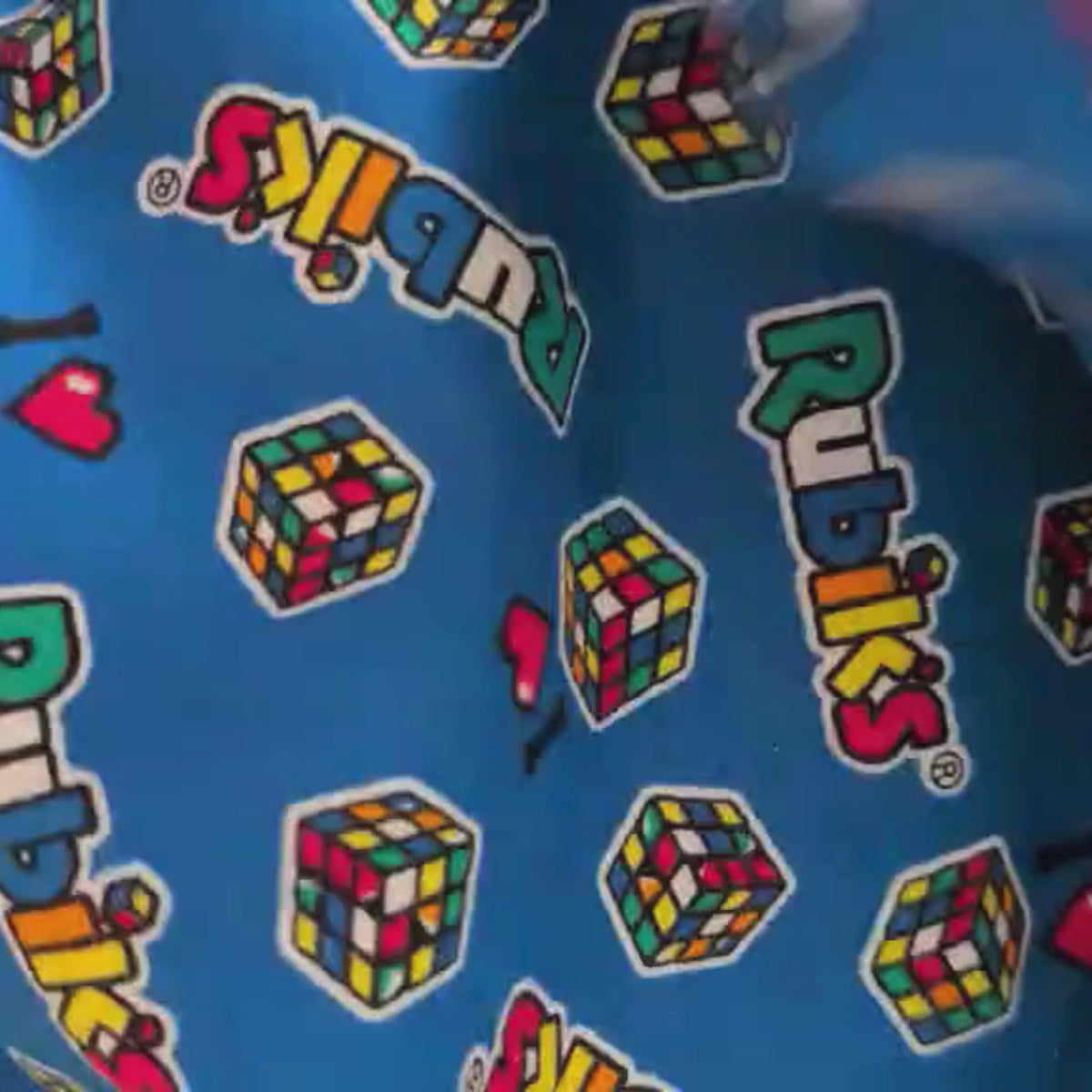 Video of Blue cotton flannel fabric featuring colorful Rubik’s Cubes and “I ♥ Rubik’s” logos, officially licensed by Camelot Fabrics