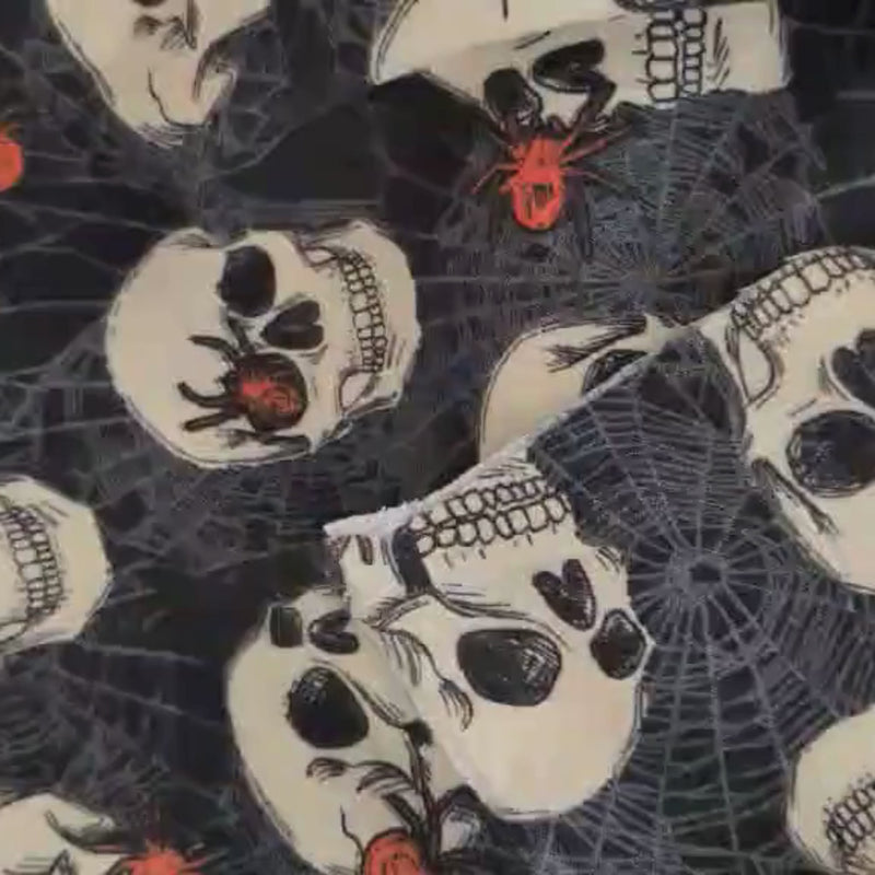 Video of Black cotton flannel fabric with ivory skulls, orange spiders, and grey spiderwebs, perfect for Halloween and horror-themed sewing projects